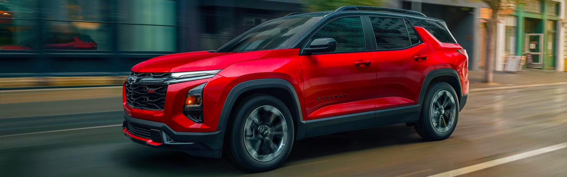 Side view of a glossy red Chevrolet Blazer EV driving on a city street with motion blur.